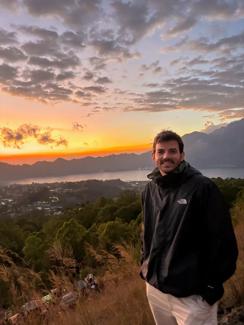 Tim on a hillside at sunset, mountains behind him and the sea below.